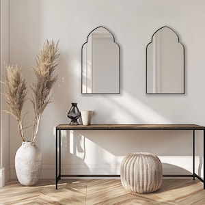 Two Accent Mirrors with black frame finish hung on the wall of an entryway over a console.