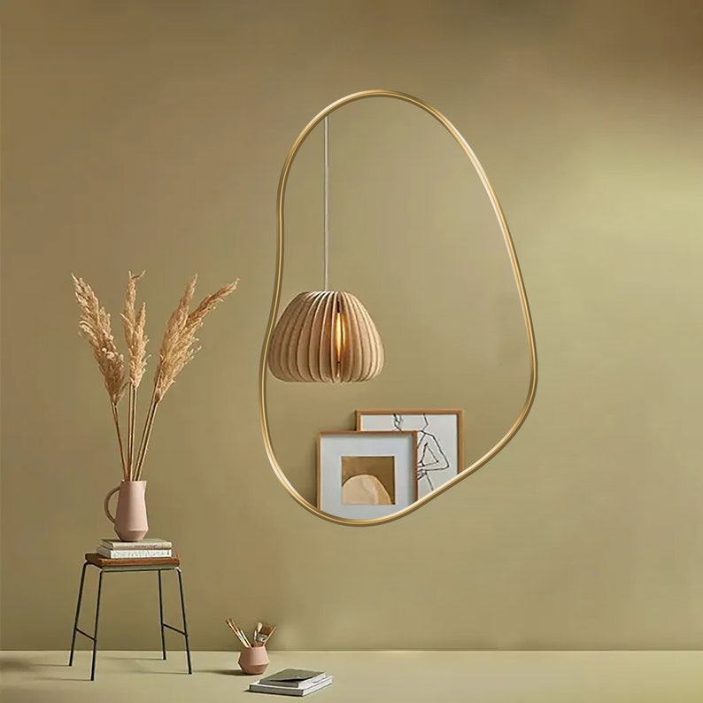 Kidney mirror with gold frame hung on the wall of a living room.