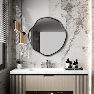 Circular Asymmetrical Mirror with Black Frame hung on the wall of a vanity room.