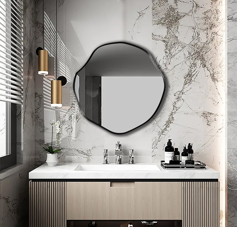 Circular Asymmetrical Mirror with Black Frame hung on the wall of a vanity room.