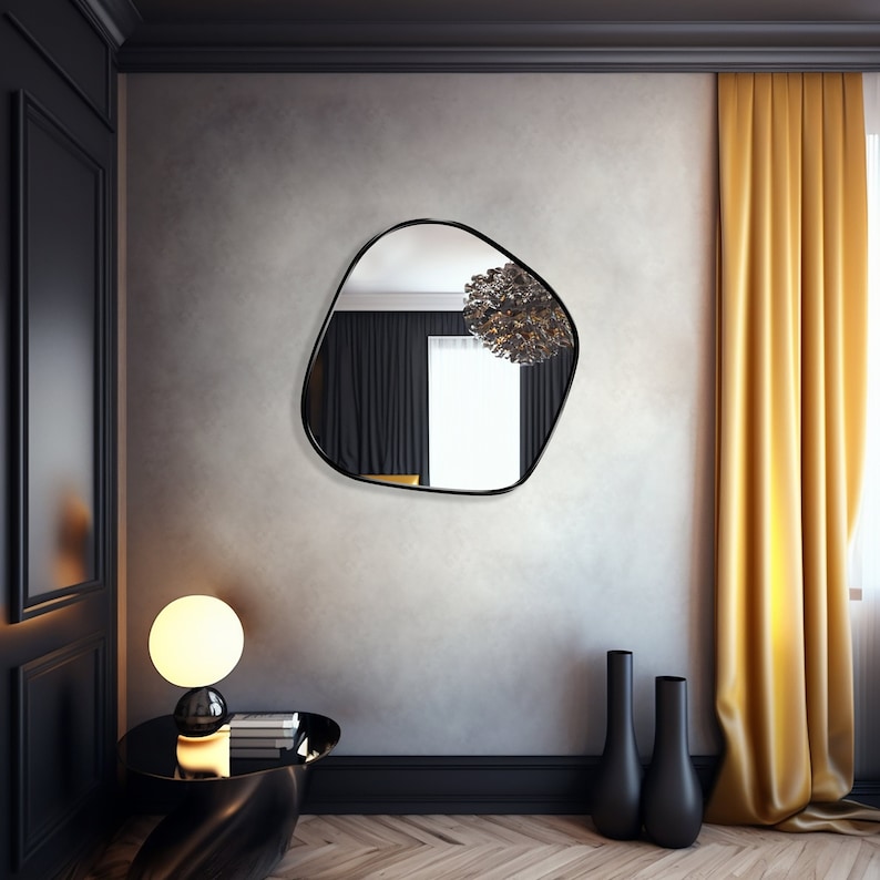 Blob shaped mirror with black frame hung on the wall of a living room.