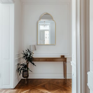 Accent Mirror with gold frame finish hung on the wall of an entryway over a console.