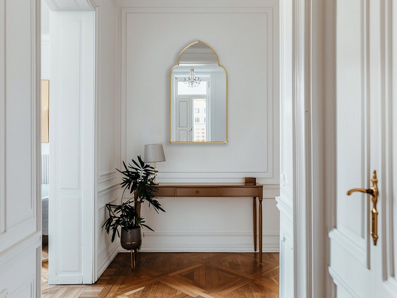 Accent Mirror with gold frame finish hung on the wall of an entryway over a console.