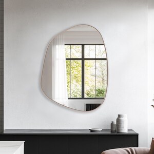 Asymmetrical Mirror with bronze frame hung on the wall of a living room over a console.