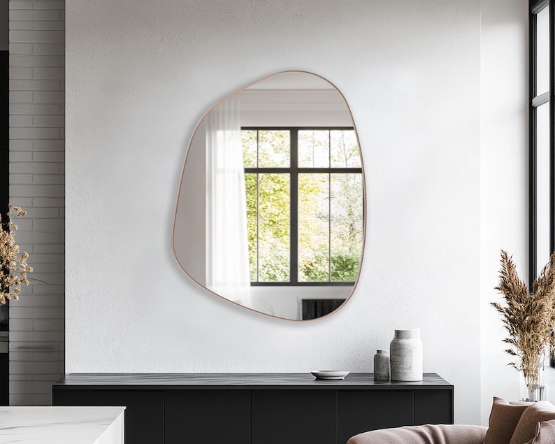 Asymmetrical Mirror with bronze frame hung on the wall of a living room over a console.