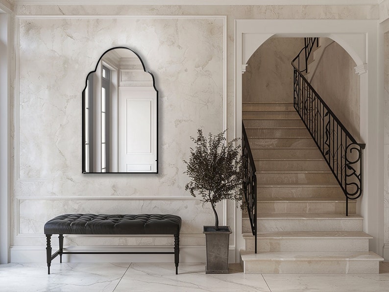 Arched Moroccan Mirror with black frame finish hung on the wall of an entryway over a bench.