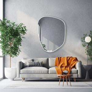 Asymmetrical mirror with white frame hung on the wall of a spacious living room over a big gray couch.