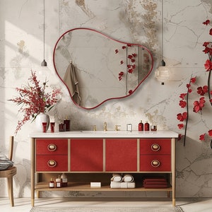 Organic Pebble Mirror with red frame finish hung on the wall of a bathroom over a red vanity with red flowers around.