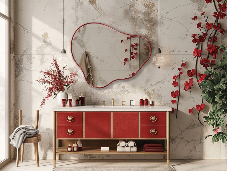 Organic Pebble Mirror with red frame finish hung on the wall of a bathroom over a red vanity with red flowers around.