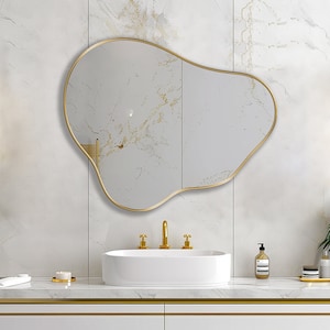 Organic Pebble Mirror with gold frame finish hung on the wall of a bathroom, over a vanity.
