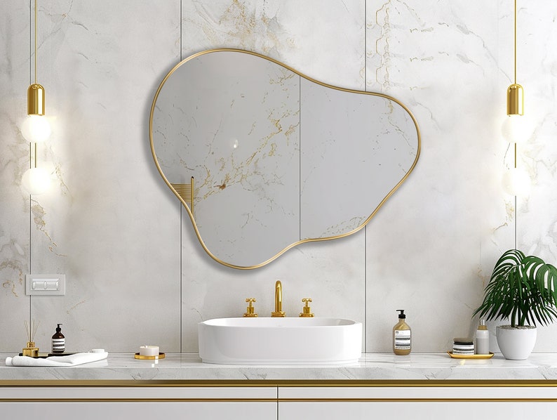 Organic Pebble Mirror with gold frame finish hung on the wall of a bathroom, over a vanity.