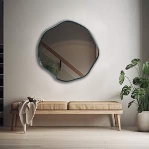 Circular Asymmetrical Mirror with emerald frame hung on the wall of an entryway.