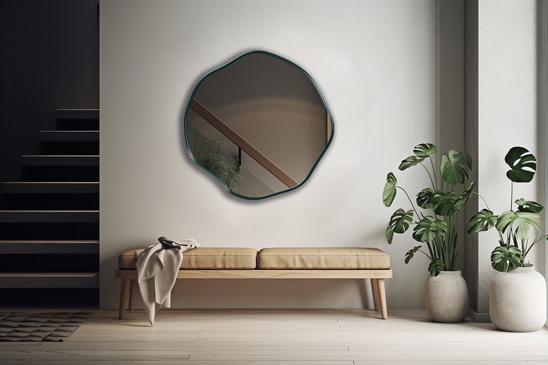 Circular Asymmetrical Mirror with emerald frame hung on the wall of an entryway.