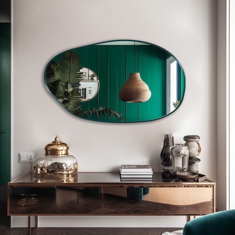 Pebble mirror with emerald frame hung on the wall of an entryway over a console.
