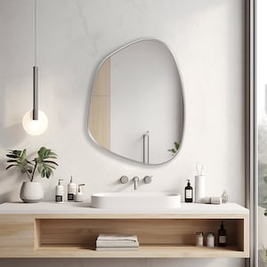 Asymmetrical mirror with silver frame hung on the wall of a bathroom over a washbasin.