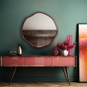 Circular Asymmetrical Mirror with red frame hung on the wall of an entryway.