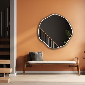 Circular Asymmetrical Mirror with white frame hung on the wall of an entryway.