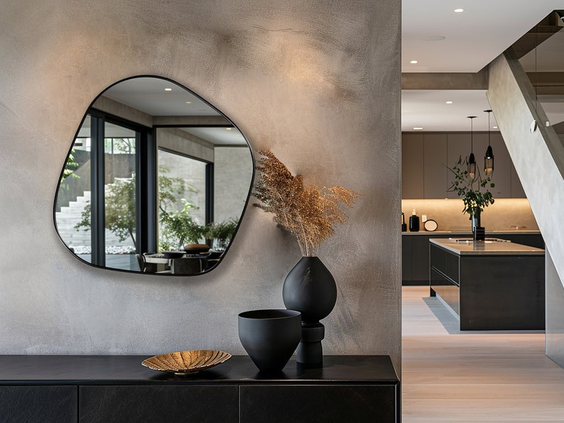 Blob shaped mirror with black frame hung on the wall of a living room.