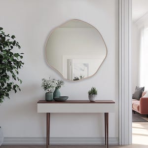 Circular Asymmetrical Mirror with bronze frame hung on the wall of an entryway over a console.