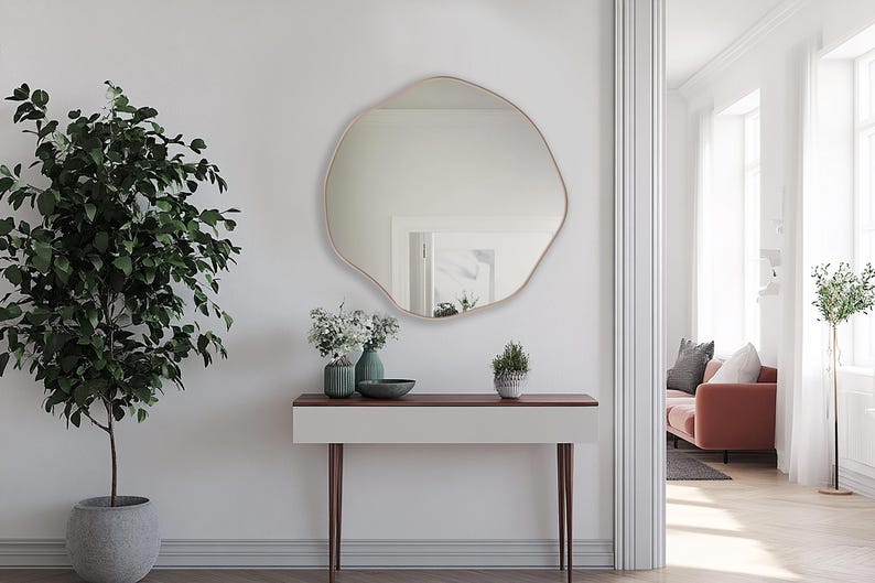 Circular Asymmetrical Mirror with bronze frame hung on the wall of an entryway over a console.