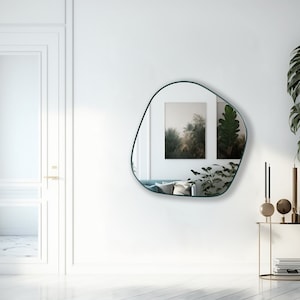 May include: A teal framed, freeform mirror hangs on a white wall above a gold metal console table with decorative objects. The mirror reflects two framed prints of nature scenes.