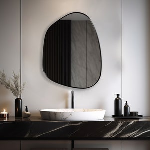 Asymmetrical mirror with black frame hung on the wall of a bathroom over a granite washbasin.