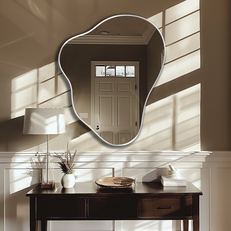 Organic Pebble Mirror with silver frame finish hung on the wall of a living room, over a console.