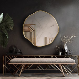 Circular Asymmetrical Mirror with gold frame hung on the wall of an entryway.