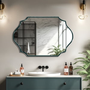 Quatrefoil mirror with emerald frame hung over the wall of a bathroom, above the bathroom vanity.