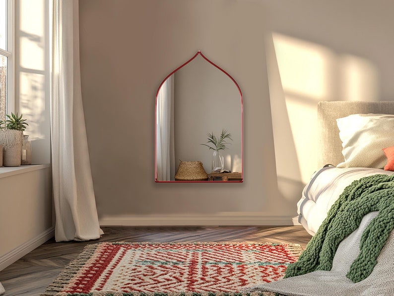 Sahara Mirror with red frame finish hung on the wall of a bedroom.