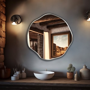 Circular Asymmetrical Mirror with silver frame hung on the wall of a bathroom.