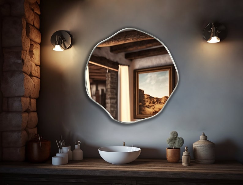 Circular Asymmetrical Mirror with silver frame hung on the wall of a bathroom.