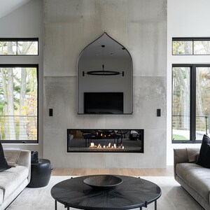 Sahara Mirror with black frame finish hung on the wall of a living room over a fireplace.