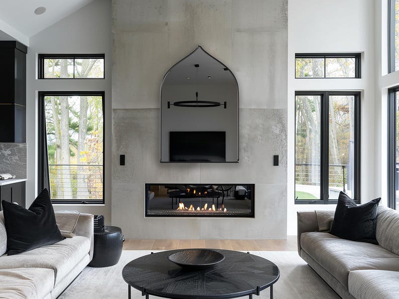 Sahara Mirror with black frame finish hung on the wall of a living room over a fireplace.