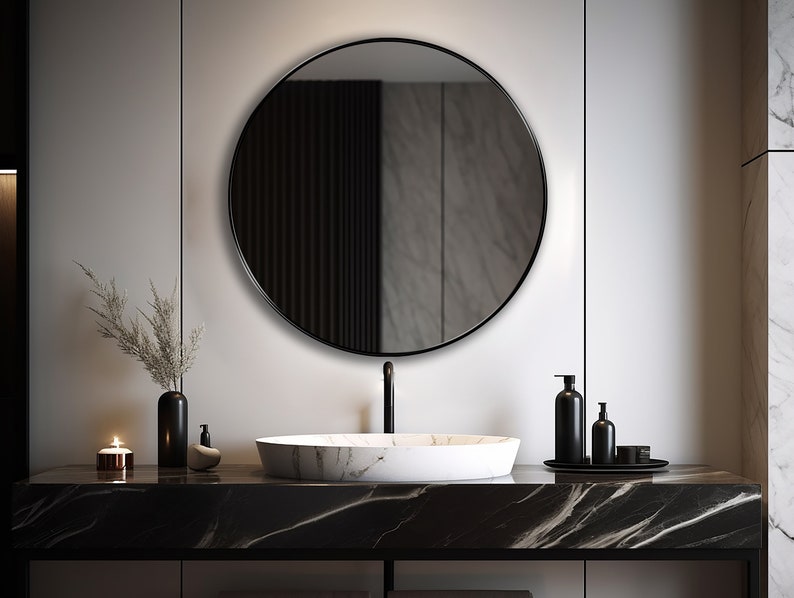 Round mirror with black finish hung on the wall of a bathroom over a vanity.