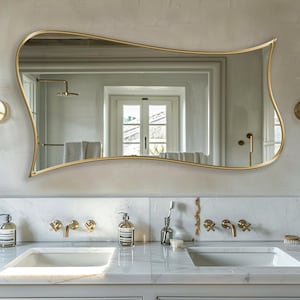 Puede incluir: Un tocador de baño de mármol blanco con dos lavabos y grifería dorada. Un espejo grande de marco dorado ondulado cuelga sobre los lavabos. Dos espejos redondos más pequeños con marcos dorados están montados en la pared a cada lado del espejo grande.