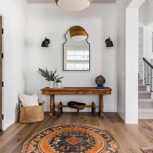 Bohemian Arched Mirror with black frame finish hang on the wall of an entryway over a wooden console.