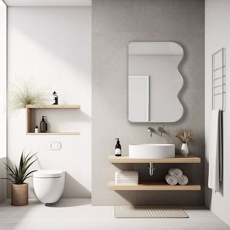 Squiggle mirror with silver frame hung on the wall of a bathroom.