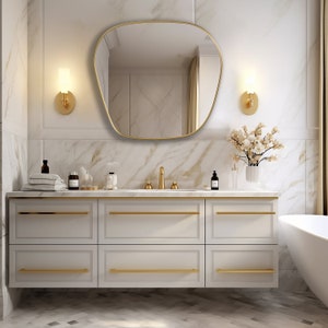 Blob mirror with gold frame finish hung on the wall of a bathroom over a vanity.