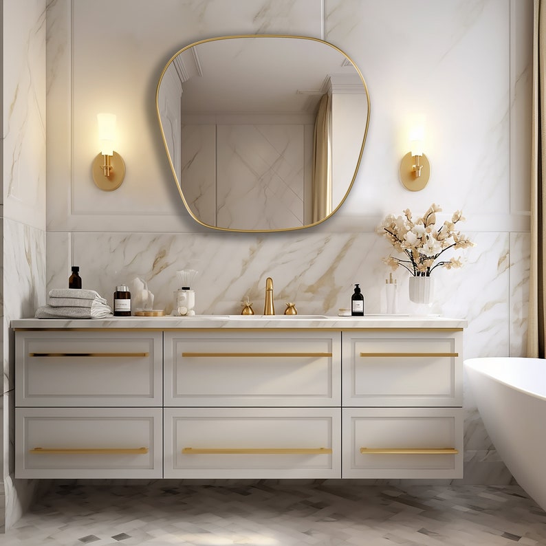 Blob mirror with gold frame finish hung on the wall of a bathroom over a vanity.