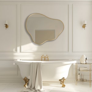 Organic Pebble Mirror with gold frame finish hung on the wall of a bathroom, over a bathtub.