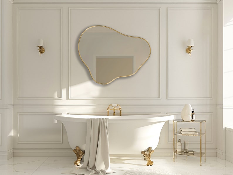 Organic Pebble Mirror with gold frame finish hung on the wall of a bathroom, over a bathtub.