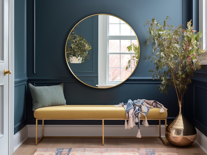 Round mirror with gold frame hung on the wall of an entryway.