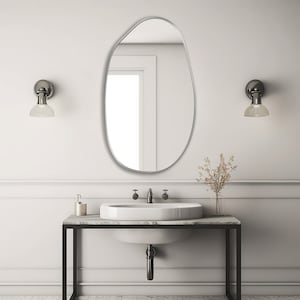 Pebble mirror with silver frame hung on the wall of a bathroom over a vanity.