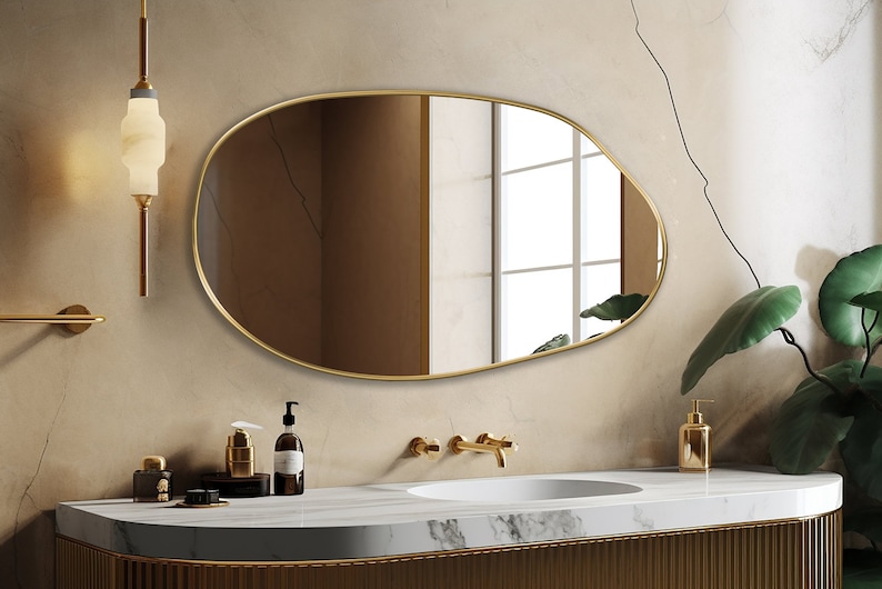 Pebble mirror with gold frame hung on the wall of a bathroom over a vanity.