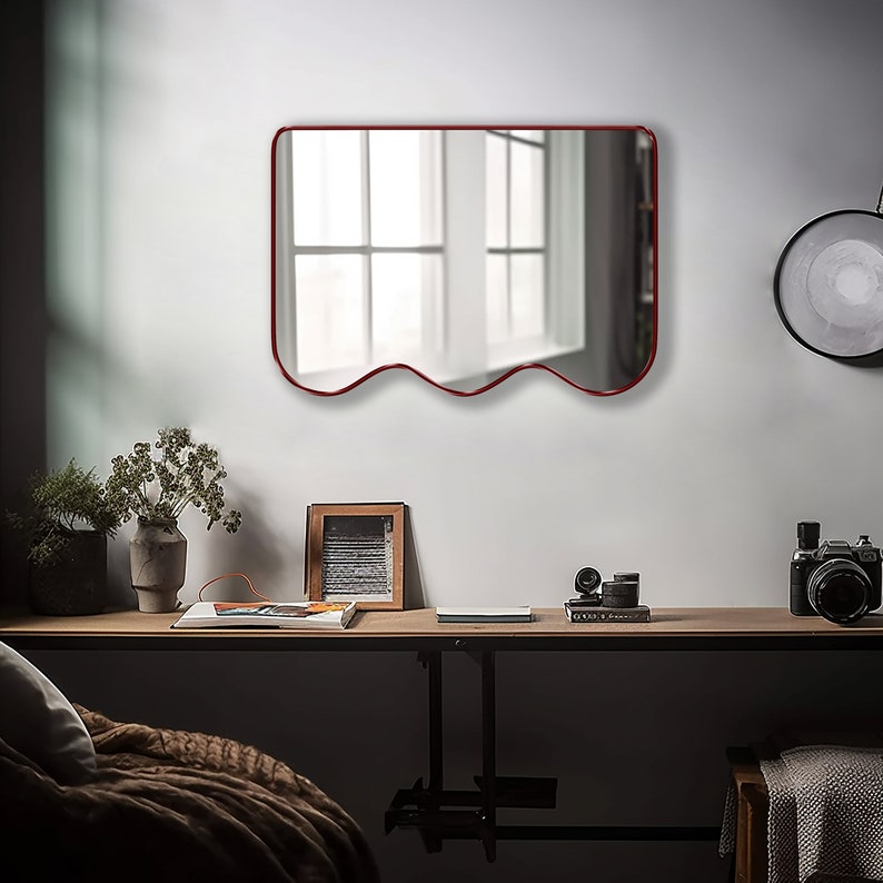 Squiggle mirror with red frame hung on the wall of a living room.