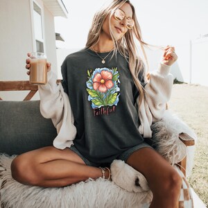 May include: A dark gray t-shirt with a pink flower graphic and the word "Faithful" printed below it.