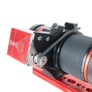Op de afbeelding: Een rode camera lens met een zwarte lensdop en een rood-wit gepatroneerd apparaat dat aan de zijkant is bevestigd.