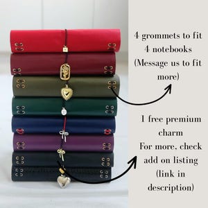 May include: A stack of eight leather-bound notebooks in red, burgundy, olive, dark green, navy, purple, and black. Each notebook features four metal grommets and a dangling metal charm. Text reads: 4 grommets to fit 4 notebooks, 1 free premium charm.