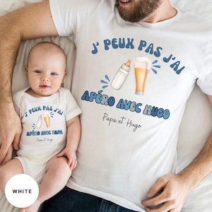 Può includere: Magliette bianche abbinate e body per bambini. La maglietta da adulto e il body per bambini hanno il testo "J' PEUX PAS J'AI APÉRO AVEC HUGO" e "J' PEUX PAS J'AI APÉRO AVEC PAPA" rispettivamente, con illustrazioni di un biberon e birra.